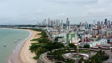 Dolly-in-aerial-drone-shot-of-a-large-round-building-on-the-beach-in-the-colorful-tropical-beach-capital-city-of-Joao-Pessoa-in-Paraiba,-Brazil-from-the-Tambaú-neighborhood-on-an-overcast-morning