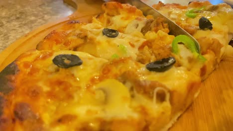 Observe-Cómo-Se-Corta-Una-Deliciosa-Pizza-En-Rebanadas-En-Un-Plato-Rústico-De-Madera,-Creando-Una-Muestra-Deliciosa-De-Ingredientes-Picantes-Y-Salados