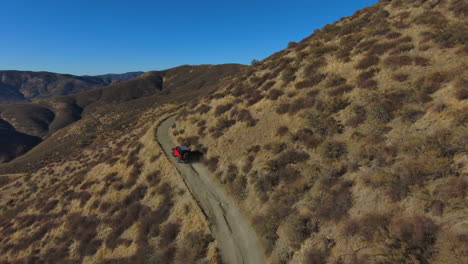 Aerial-drone-tracking-shot-of-red-jeep-driving-on-hill-desert-landscape-road