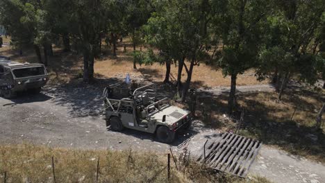 Israel-Army-infantry-squad-soldiers-on-vehicle-driving-through-green-field-at-training-ground-country-road,-Aerial-Tracking-shot