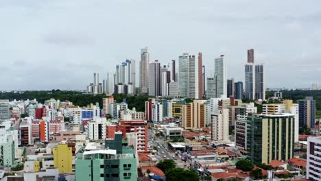 Descending-aerial-drone-shot-of-the-colorful-tropical-beach-capital-city-of-Joao-Pessoa-in-Paraiba,-Brazil-from-the-Tambaú-neighborhood-on-an-overcast-morning-with-traffic-below-and-skyscrapers-above