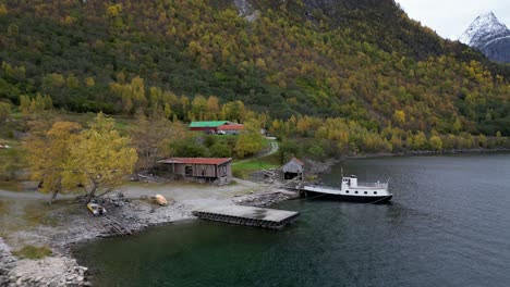 Drone-flies-between-old-boathouse-and-sawmill-on-Vike-in-Eikesdsal,-in-Molde-municipality-in-Norway
