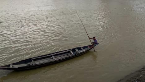 Eine-Fesselnde-Aufnahme-Eines-Holzbootes,-Das-Auf-Einem-Fluss-In-Asien-Schwimmt,-Mit-Einem-Erfahrenen-Bootsmann,-Der-Durch-Das-Wasser-Rudert-Und-Navigiert