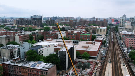 Aerial-view-overlooking-a-crane-lifting-materials-at-a-construction-site-at-a-train-station-in-cloudy-Harlem,-NYC