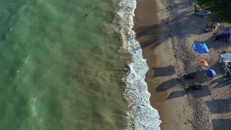Rising-bird's-eye-drone-shot-of-Penha-beach-coastline-near-the-capital-city-of-Joao-Pessoa-in-Paraiba,-Brazil-with-waves-crashing-into-the-sand-and-people-playing-in-the-water-and-relaxing