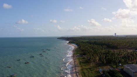 Dolly-out-aerial-drone-shot-of-the-beautiful-tropical-Penha-beach-coastline-near-the-capital-city-of-Joao-Pessoa-in-Paraiba,-Brazil-with-waves-crashing-into-the-sand-and-small-fishing-boats-docked
