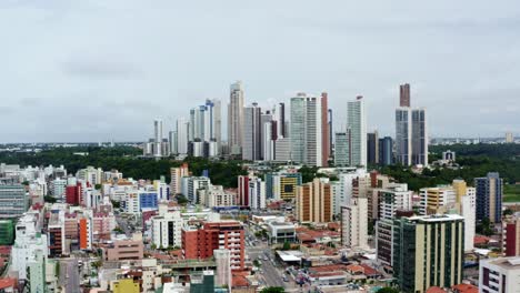 Dolly-in-aerial-drone-shot-of-the-colorful-tropical-beach-capital-city-of-Joao-Pessoa-in-Paraiba,-Brazil-from-the-Tambaú-neighborhood-on-an-overcast-morning-with-traffic-below-and-skyscrapers-above