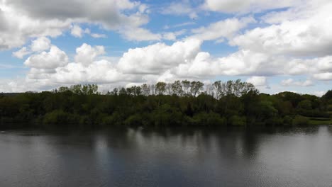 Aerial-forward-rising-shot-over-a-lake-towards-trees-at-Chard-Reservoir-in-Somerset-South-West-England-with-dramatic-clouds