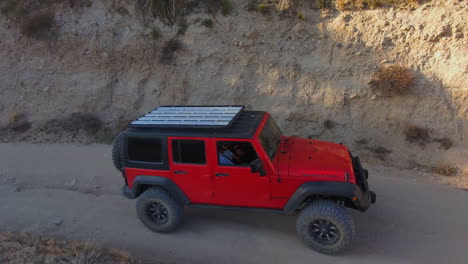 Epic-aerial-drone-view-of-Red-jeep-riding-off-dirt-road-in-desert-hills