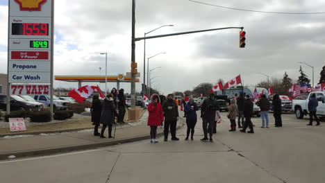 Protestors-holding-American-and-Canadian-flags-near-a-gas-station,-standing-up-for-democracy-and-political-activism