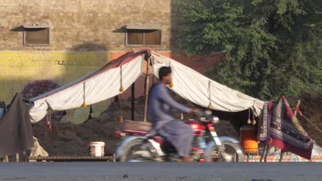 Campamento-Improvisado-Al-Borde-De-La-Carretera-Realizado-Por-Locales-Debido-A-Las-Inundaciones-En-Sindh,-Pakistán,-Con-Tráfico-Pasando
