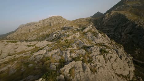 FPV-drone-shot-over-snake-road-going-under-an-overbridge-through-rocky-mountain-range-in-Sa-Calobra,-Mallorca,-Spain-at-daytime