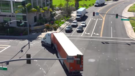 Aerial-tracking-Schneider-National-Truck-on-city-road-as-truck-goes-through-intersection,-gorilla-style-shoot