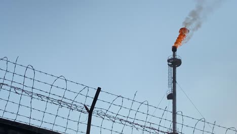 Telephoto-close-up-of-burning-Gas-Flare-also-known-as-flare-stack,-behind-wall