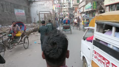 First-person-view-from-a-rickshaw-passenger-seat-as-a-rickshaw-puller,-or-driver,-rides-through-the-busy-streets-of-Dhaka,-Bangladesh