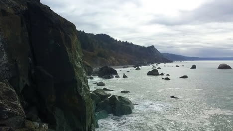 Drone-shot-of-cliffs-and-rocky-ledges-with-evergreens-and-ocean,-Pacific-Northwest