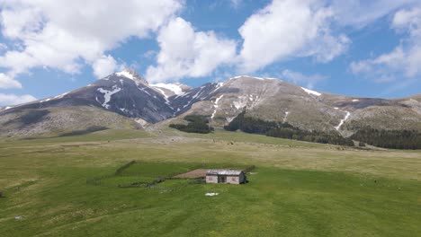 Wide-angle-scene-of-an-old-Sheppards-shelter-in-a-grassland-valley-surrounded-by-the-Gran-Sasso-mountain-range-in-the-rural-countryside-of-Abruzzo-in-Italy