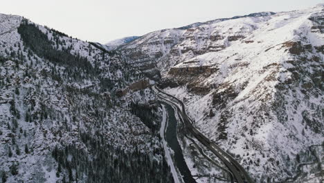 Drone-dolley-tilt-shot-of-Colorado-river-streaming-next-to-a-highway-through-the-Glennwood-Canyon-in-winter