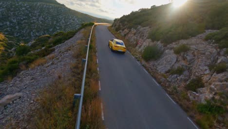 Scenic-FPV-aerial-following-a-yellow-sportscar-driving-along-the-side-of-a-mountain-in-Catalonia,-Spain