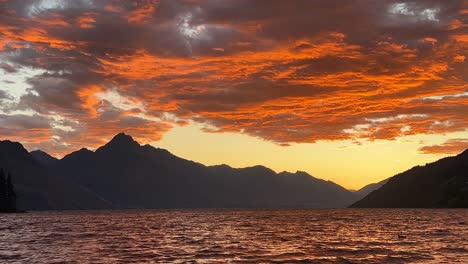 Stunningly-coloured-orange-clouds-above-lake-Wakatipu-during-a-summer-sunset-in-Queenstown,-New-Zealand