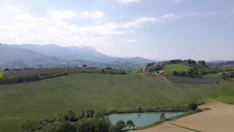 Wide-angle-drone-shot-of-a-stunning-scene-of-a-valley-with-farmland,-wineries-and-the-Gran-Sasso-mountain-range-in-the-distance-located-in-the-countryside-of-Abruzzo-in-Italy