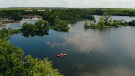 Aerial-drone-orbit-over-lone-fisherman-in-kayak-on-serene-lake-water