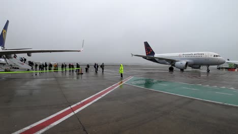 Avión-De-Brussels-Airlines-Rodando-Hasta-La-Puerta-Del-Aeropuerto,-Pasajeros-De-Ryanair-Haciendo-Cola-Para-La-Salida-Del-Vuelo---Aeropuerto-De-Bruselas,-Bélgica