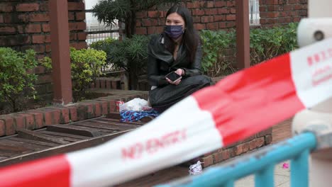 Eine-Frau-Mit-Gesichtsmaske-Sitzt-Neben-Einem-Geschlossenen-öffentlichen-Spielplatz-Aufgrund-Des-Ausbruchs-Des-Covid-19-Coronavirus-Und-Der-Beschränkungen-In-Hongkong