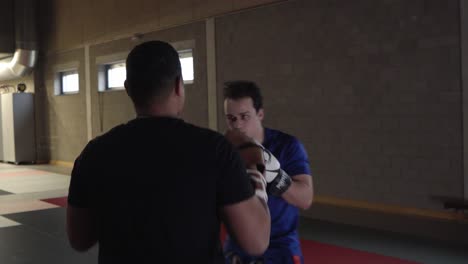 Zwei-Amateurboxer-Trainieren-Im-Indoor-Fitnessstudio-Und-üben-Dabei-Schläge-Auf-Die-Handschuhe