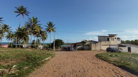 Slow-motion-shot-moving-down-a-small-cobblestone-road-with-palm-trees-and-a-view-of-the-ocean-from-the-Barra-de-Cunhaú-in-the-small-town-of-Canguaretama-in-Rio-Grande-do-Norte,-Brazil-on-a-summer-day