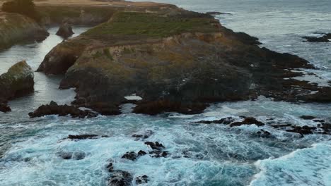 Rising-drone-shot-of-California's-eroding-coastline,-starting-on-water-and-ending-on-a-steep-hillside