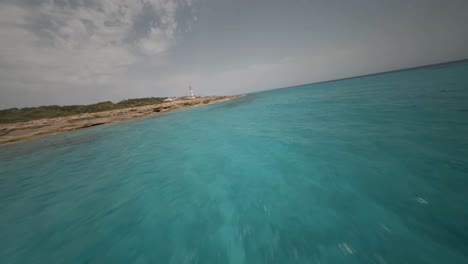 FPV-drone-shot-over-amazing-landscape-with-beautiful-turquoise-colored-sea-water-along-rocky-beach-with-lighthouse-over-the-beach
