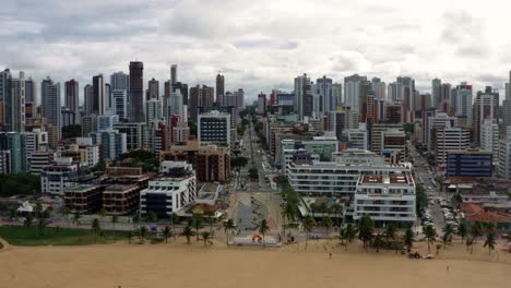 Dolly-in-aerial-drone-shot-of-the-famous-tourist-destination-Tambaú-beach-in-the-tropical-capital-city-of-Joao-Pessoa-in-Paraiba,-Brazil-with-golden-sand-surrounded-by-large-buildings-and-skyscrapers