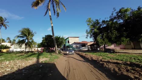 Slow-motion-shot-moving-down-a-small-dirt-road-surrounded-by-palm-trees-from-the-Barra-de-Cunhaú-in-the-small-town-of-Canguaretama-in-Rio-Grande-do-Norte,-Brazil-on-a-summer-day