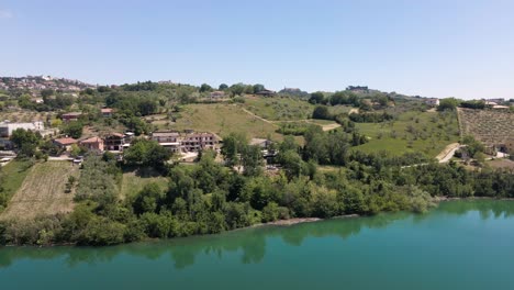 Drone-shot-of-a-rural-village-near-Penne-revealing-a-beautiful-emerald-lake-in-the-remote-countryside-of-Abruzzo-in-Italy