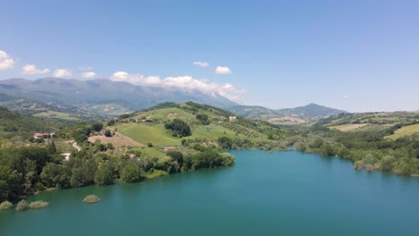 Wide-angle-drone-shot-of-a-beautiful-panorama-view-of-an-emerald-lake-located-in-a-valley-surrounded-by-a-mountain-range-and-farmland-in-the-countryside-of-Abruzzo-in-Italy