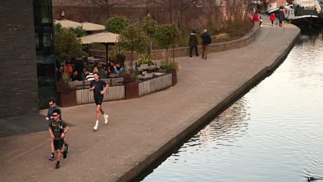 People-running-along-Regents-Canal-at-the-weekend-past-the-Coal-Drops-Yard,-London,-United-Kingdom