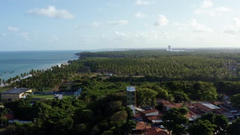 Dolly-in-aerial-drone-shot-of-the-stunning-tropical-coastline-of-Paraiba,-Brazil-near-the-beach-capital-of-Joao-Pessoa-near-a-residential-area-with-dense-exotic-foliage-and-palm-trees-below