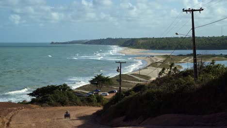 Gramame-beach-where-the-ocean-meets-the-large-river-with-waves-crashing-into-the-sand-and-a-four-wheeler-driving-down-the-dirt-road,-near-the-beach-capital-city-of-Joao-Pessoa-in-Paraiba,-Brazil