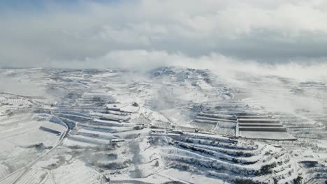 Aerial-view-of-snow-covered-village-and-terraced-farmland-under-heavy-clouds,-Israel