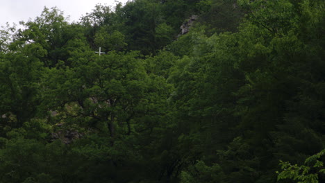 White-holy-cross-concealed-by-trees-on-steep-forest-hillside-cliff