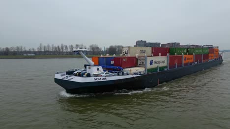 Luftverfolgungsaufnahme-Von-Der-Backbordseite-Des-Containerschiffs-Scaldis,-Das-An-Einem-Bewölkten-Tag-In-Dordrecht-Entlang-Der-Oude-Maas-Fährt