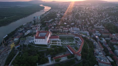 Aerial-footage-of-Bratislava-sunset,-panning-down-to-castle-with-river-crossing-the-frame