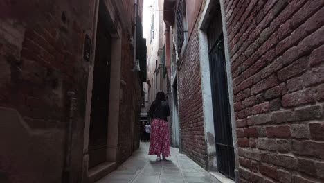 Vista-Posterior-De-Una-Mujer-Del-Sur-De-Asia-Caminando-Por-Callejones-Con-Estructuras-De-Paredes-De-Ladrillo-En-Venecia,-Italia