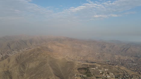 Aerial-Shot-Of-Lima-Houses-On-Dust-Mountains-Under-Cloudy-Blue-Sky,-Peru