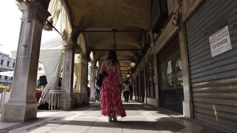 Mujer-Vestida-Caminando-Por-Un-Callejón-Cubierto-A-Lo-Largo-De-Los-Puestos-En-Venecia,-Italia