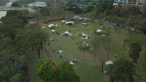 Campamento-De-Tiendas-Con-Gente-Haciendo-Un-Picnic-Al-Aire-Libre-En-Una-Tarde-De-Fin-De-Semana-En-El-área-Del-Parque-Verde