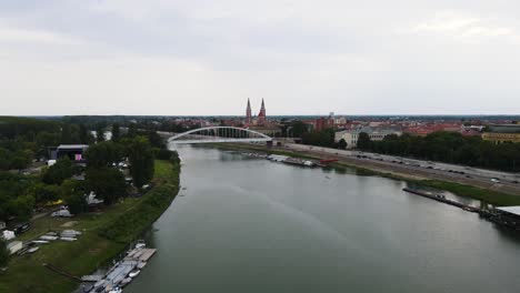 Flyover-above-Tisza-River-towards-Belvárosi-Bridge,-Votive-Church-in-Szeged,-Hungary