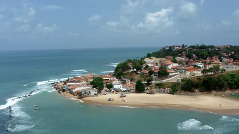 Dolly-out-rotating-aerial-drone-wide-shot-of-the-tropical-famous-Baia-Formosa-beach-town-in-the-state-of-Rio-Grande-do-Norte,-Brazil-with-fishing-boats,-coastal-homes,-small-waves,-and-surfers