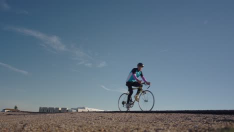 Cyclist-riding-bike-on-empty-road,-low-angle-front-view,-blue-sky,-slow-motion